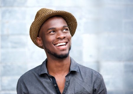 close up portrait of a happy young african american man laughing against gray background