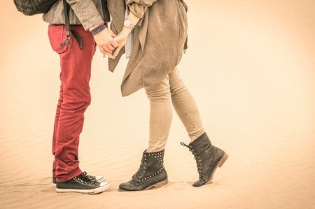 concept of love in autumn - couple of young lovers kissing outdoors with closeup on legs and shoes - desaturated nostalgic filtered look